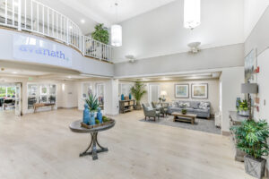 Interior Vistas at Lake Largo apartments Lobby/Office, White walls, avanath signage under second story railing, rustic decorr, leasing office to the right upon entering lobby, landscape paintings on walls of lobby, wood floors.