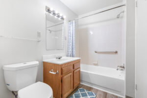 Interior Unit Bathroombathttub/shower, light brown cabinets, white countertop, vanity mirror, wood floors, white walls.